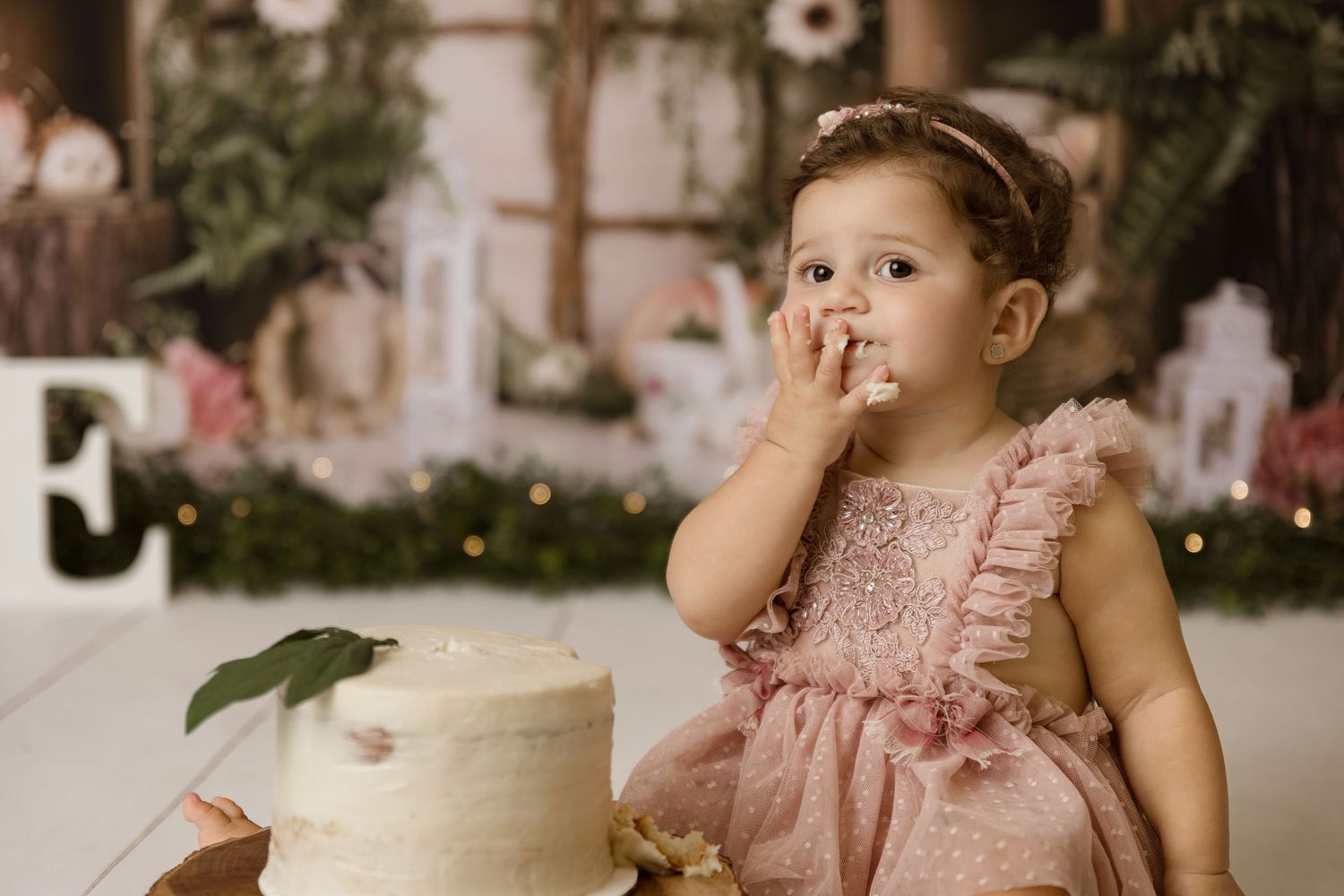 Toddler tasting frosting beside a white cake in a rustic first birthday set