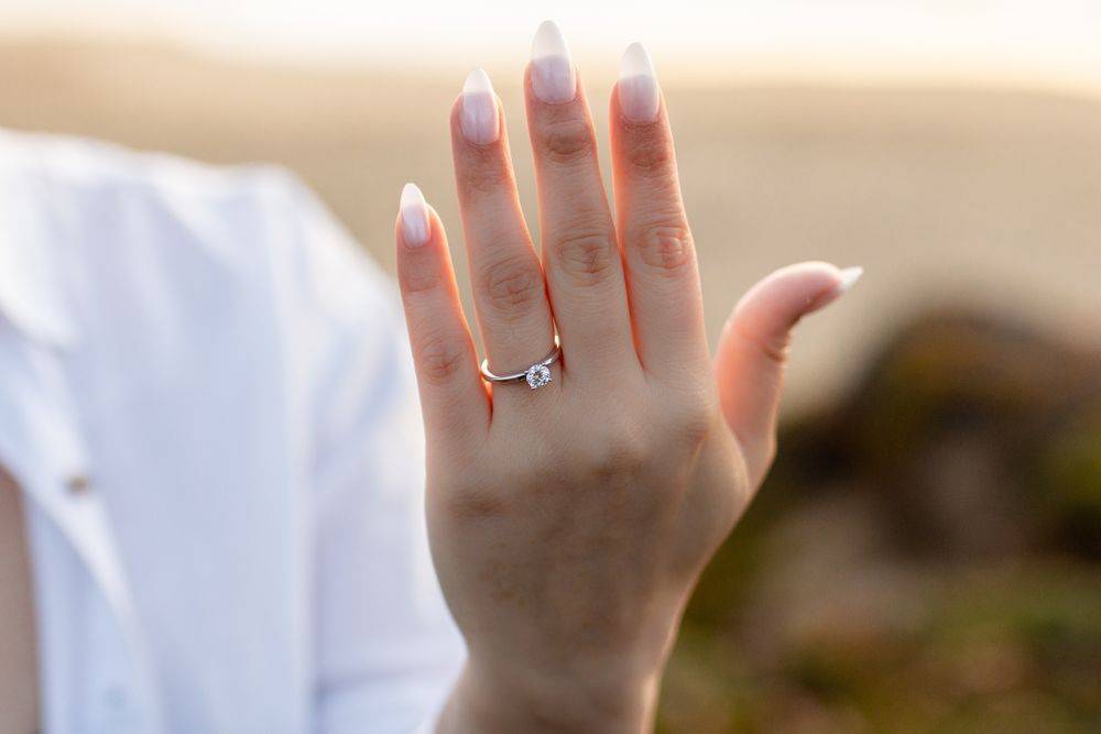 Close-up of a woman's hand displaying a elegant solitaire diamond engagement ring with French manicure nails.