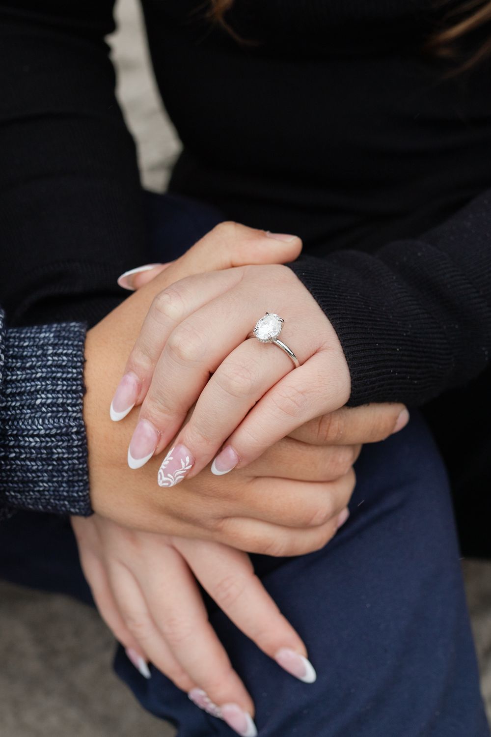 Close-up of hands holding with a stunning oval diamond solitaire engagement ring on French manicured nails.