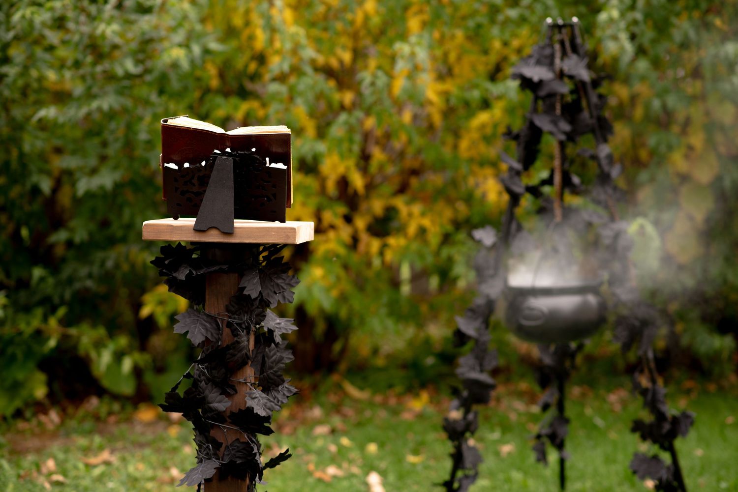 Halloween decorations with a spellbook on a post and a smoking cauldron on a stand in an autumn garden.