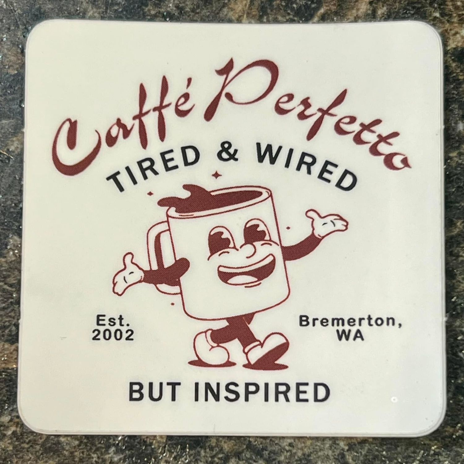 Caffe Perfetto ceramic coaster, Tired & Wired But Inspired, Est. 2002 Bremerton WA, featuring a smiling coffee cup mascot.