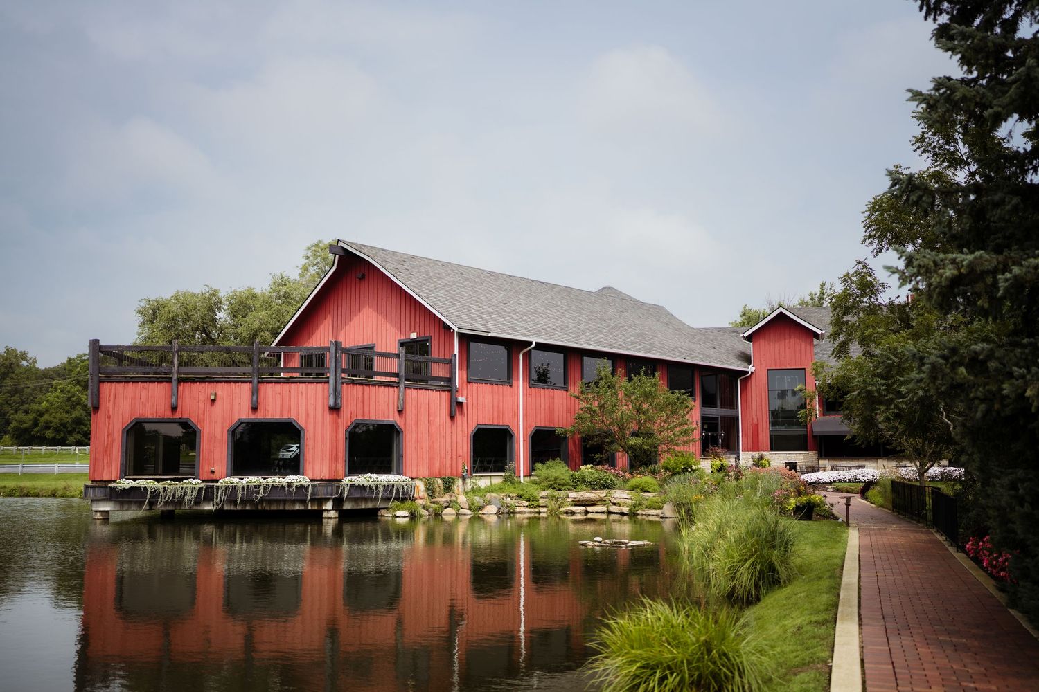Red barn building reflected in a serene pond surrounded by lush greenery and a brick walkway.