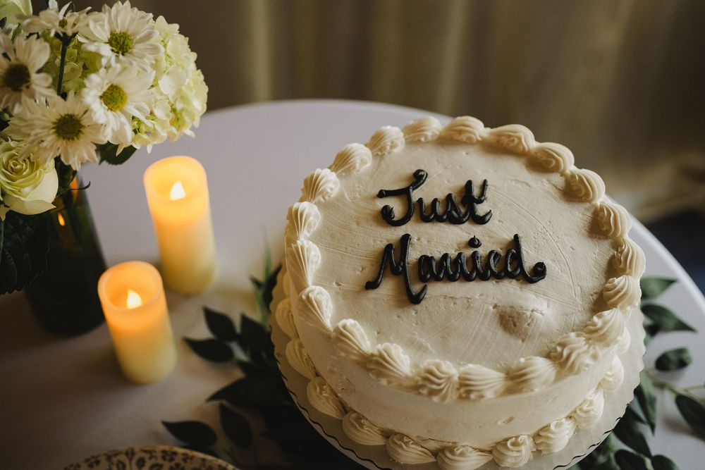Just Married white wedding cake with cream rosettes beside candles and white flowers.