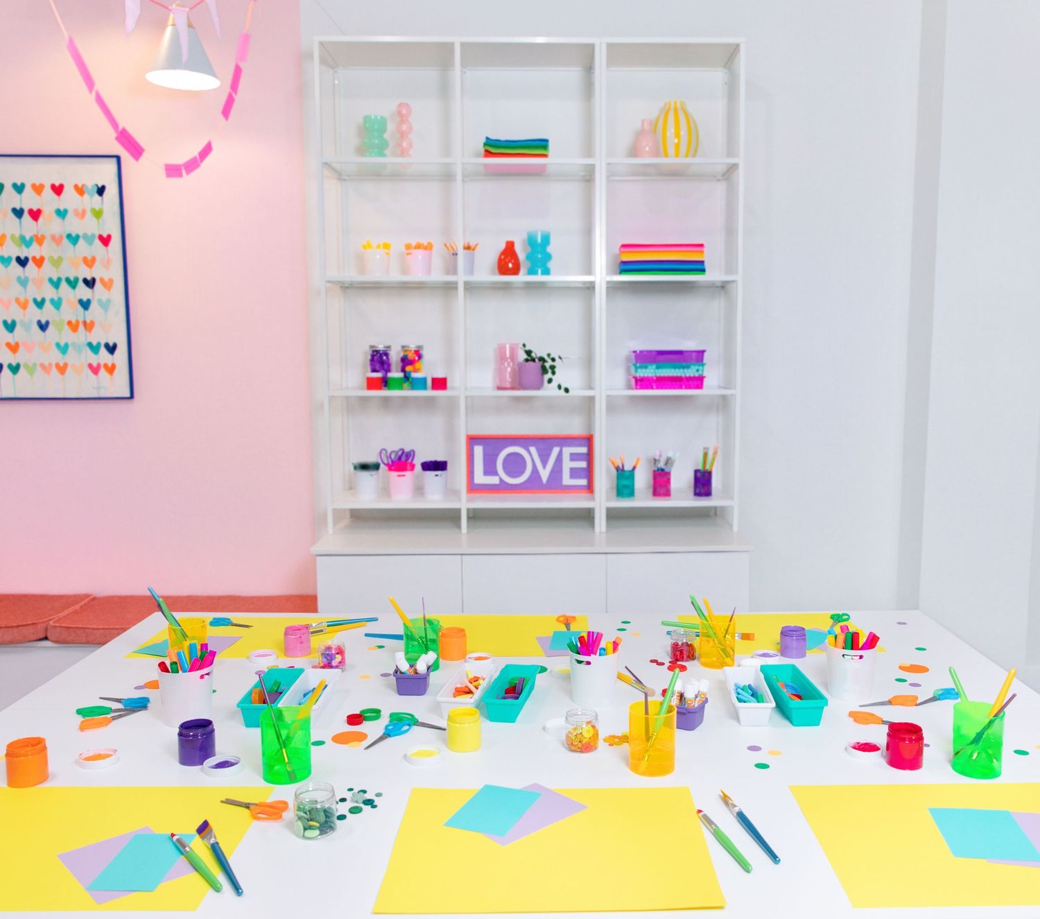 Colorful art studio with pink walls, white shelves, and vibrant supplies including pencils, paper, and a LOVE sign.