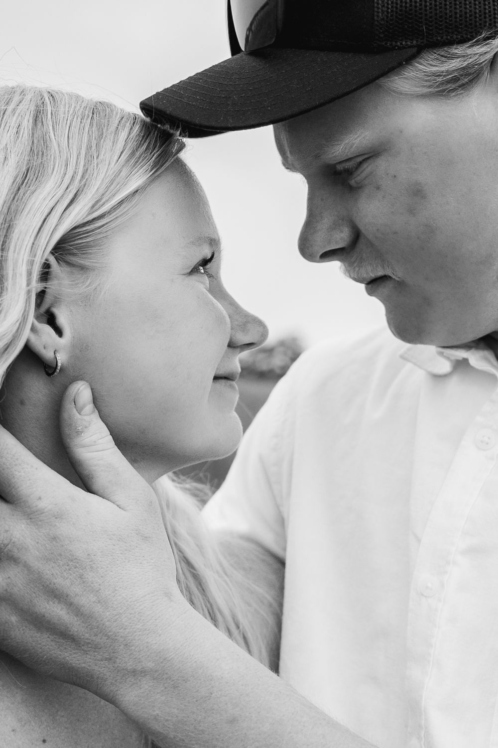 Black and white photo of a couple sharing a tender moment, man in baseball cap gently holding womans face.