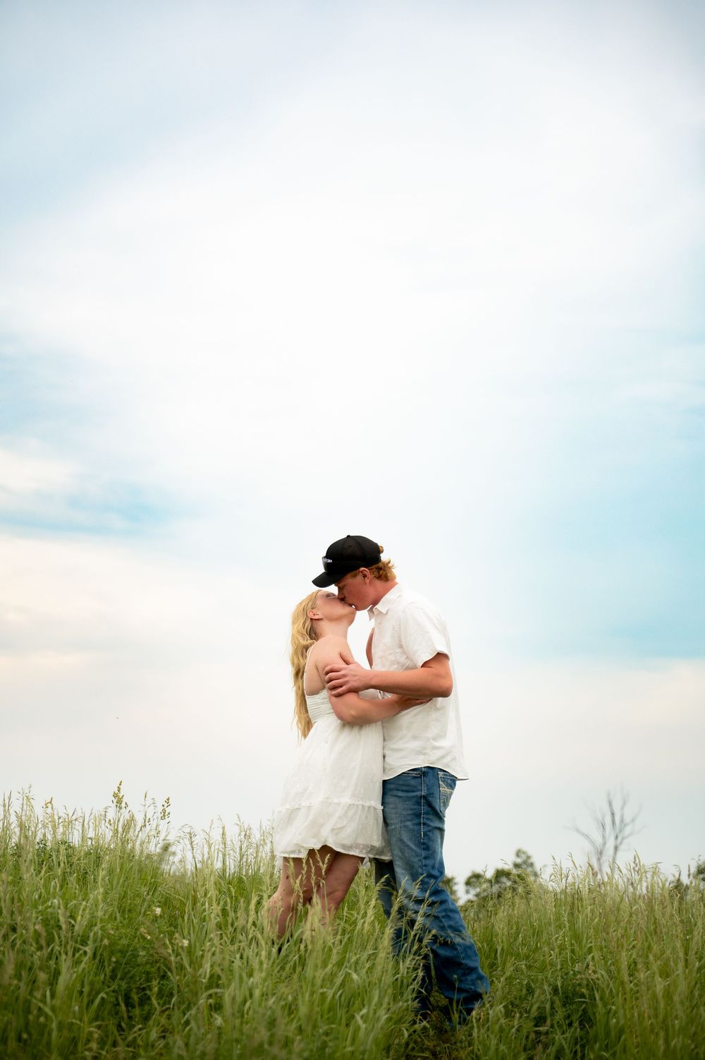 Young couple sharing a romantic kiss in a lush green meadow under a cloudy sky.