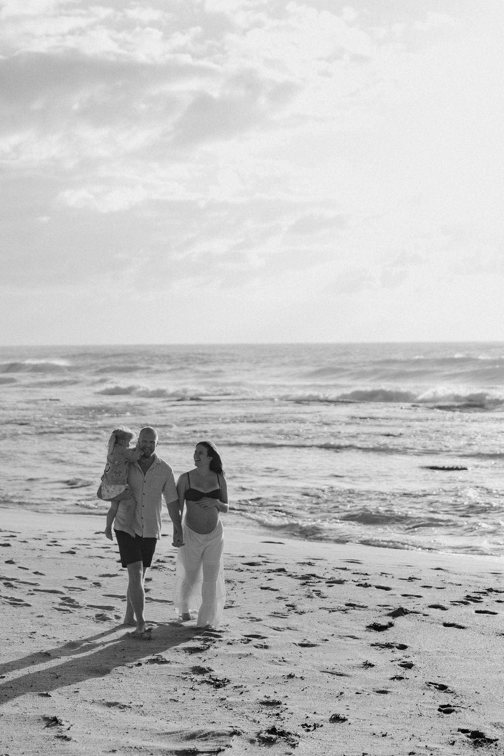 Black and white photo of a family walking along a sandy beach with ocean waves in the background.