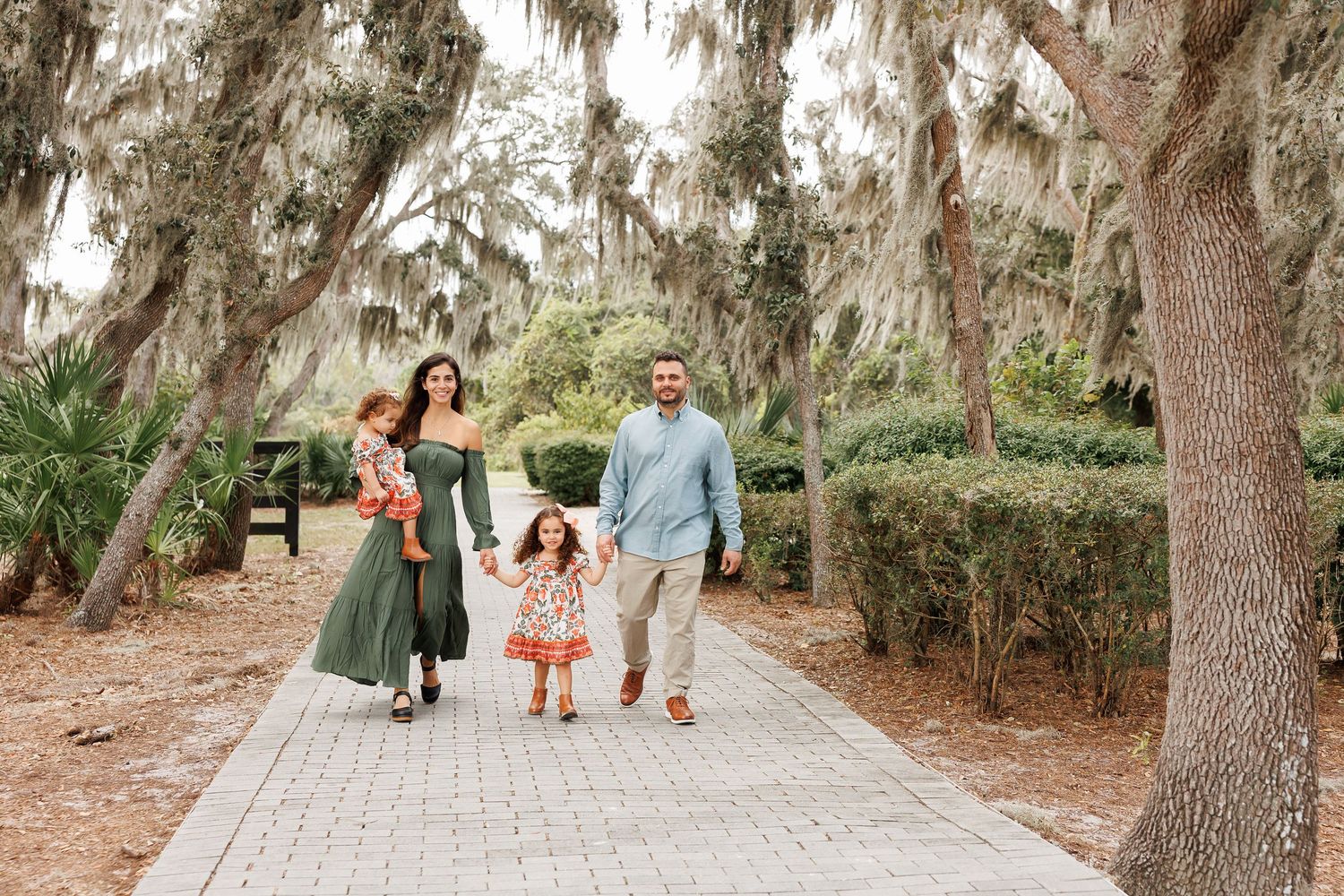 A scenic path through moss-draped oak trees creates a natural tunnel effect in a wooded area.