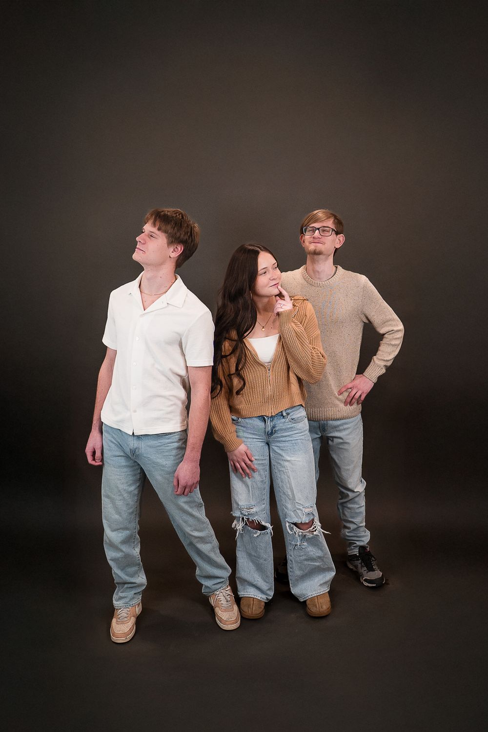Three young adults in jeans pose against a dark background, two looking up and one gazing thoughtfully ahead.