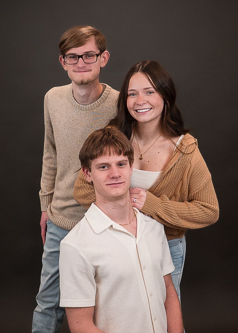 Three smiling young adults pose together for a professional studio portrait against a dark gray background.