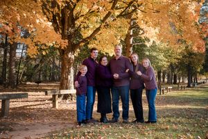 Family of six poses under vibrant autumn trees in a park, wearing coordinating purple and blue outfits.