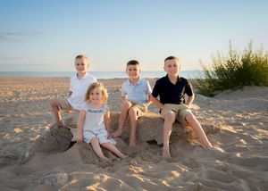 Four children smile together on a sandy beach, sitting on a sandcastle at golden hour.