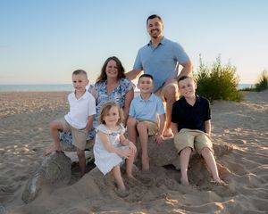 Family of six poses on sandy beach at sunset, parents with four children smiling for a portrait.