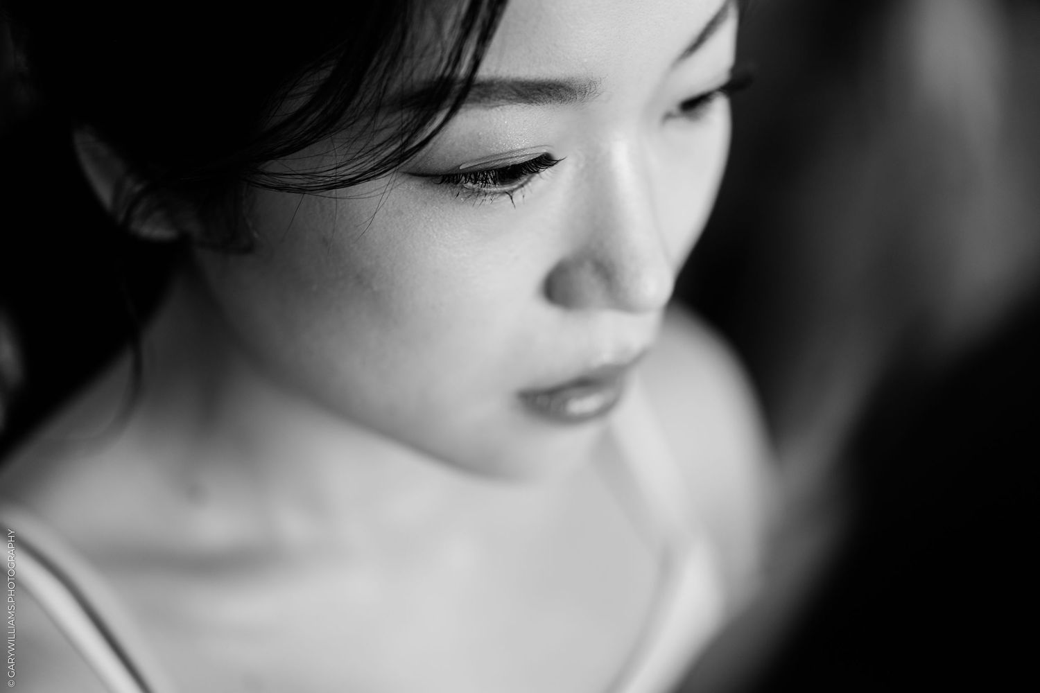 Black and white close-up portrait of a young Asian woman looking down with elegant makeup and delicate features.