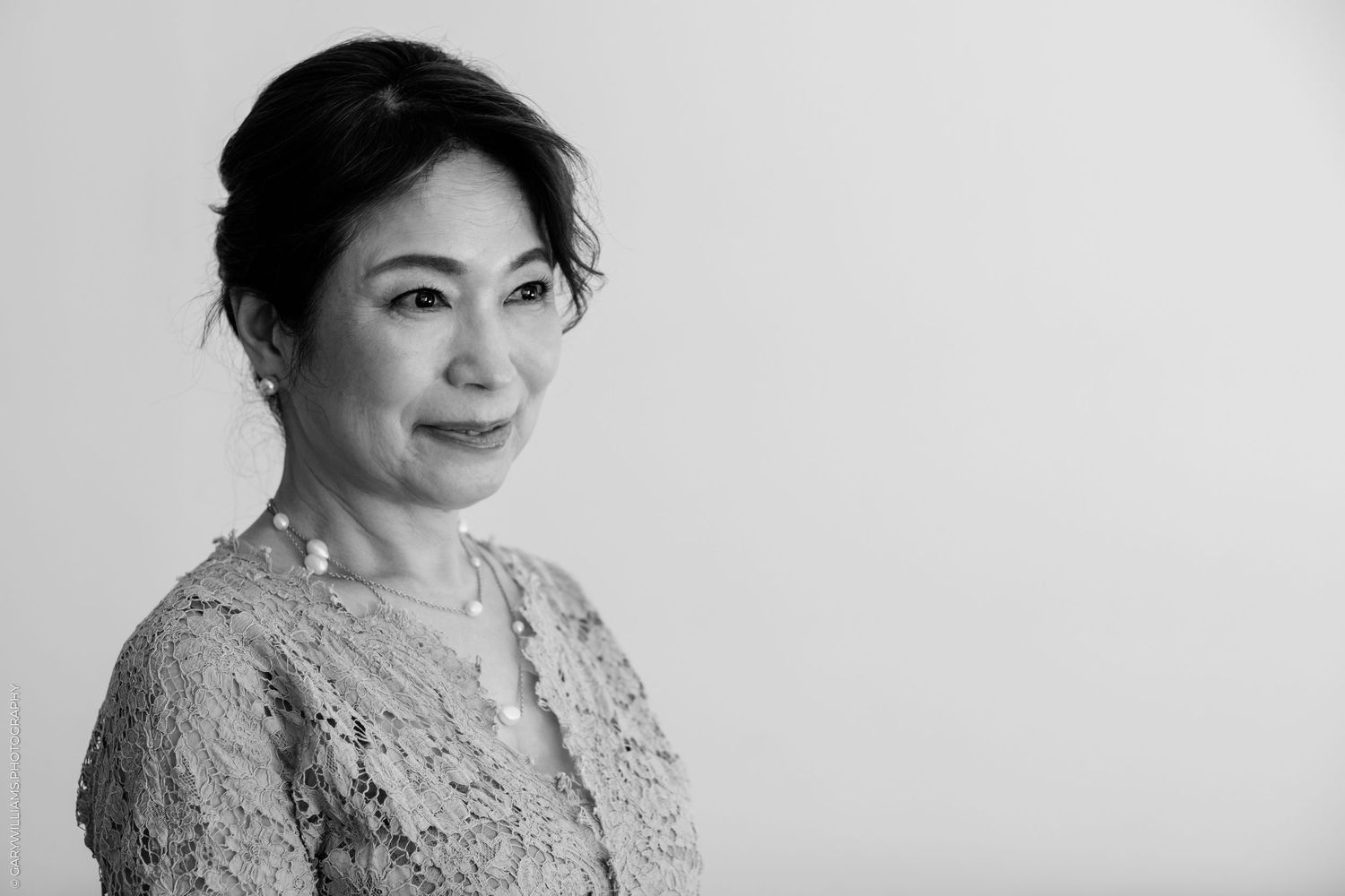 Black and white portrait of a smiling middle-aged Asian woman in lace top with hair up.