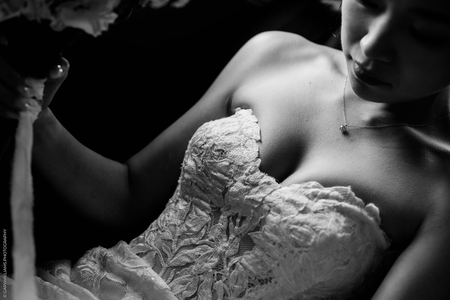 Black and white photo of a bride in a strapless lace wedding gown holding a bouquet, elegant necklace visible.