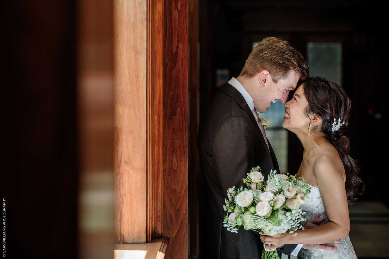 Bride and groom share a romantic moment, nearly kissing, as bride holds a white bouquet in an elegant wedding setting.