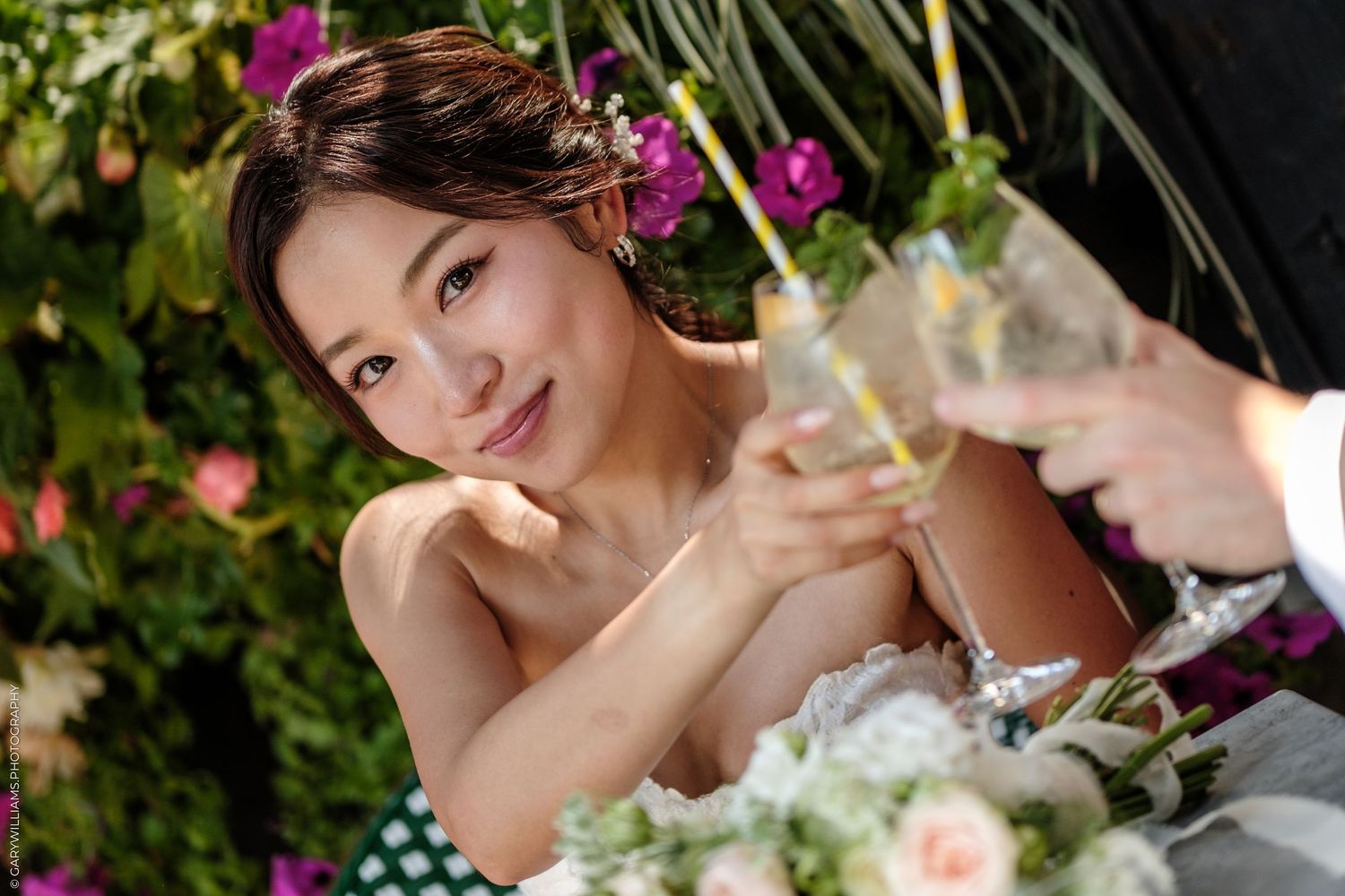 Smiling bride in white dress toasting with champagne glass at floral wedding reception.
