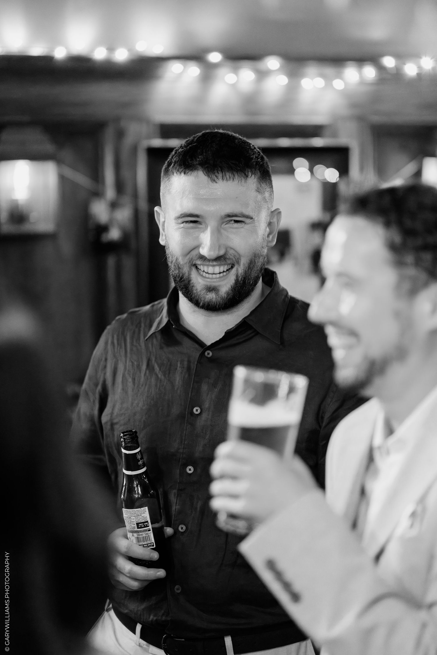 Two men laughing and holding drinks at a party, captured in black and white photography.