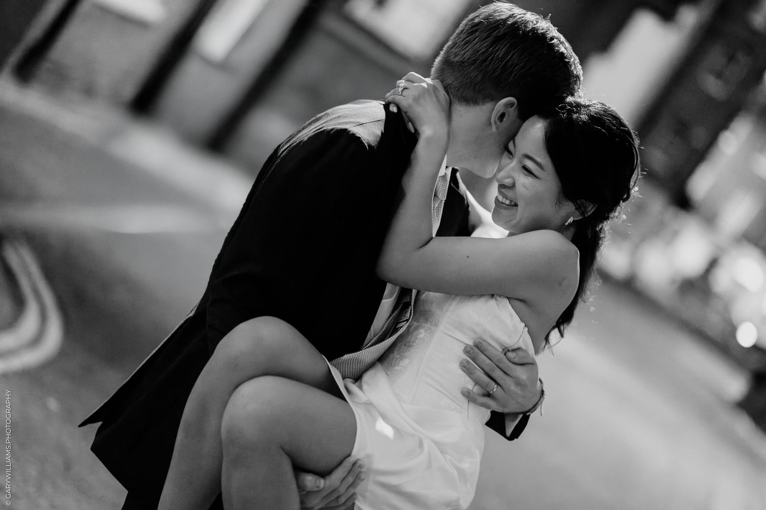 Black and white photo of a couple sharing a romantic embrace outdoors on their wedding day.