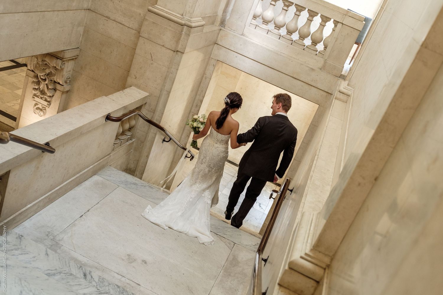 Bride and groom walking up marble staircase in elegant venue on their wedding day.