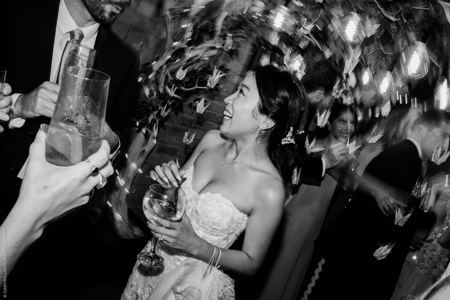 Black and white photo of a smiling bride dancing under confetti at her wedding reception.