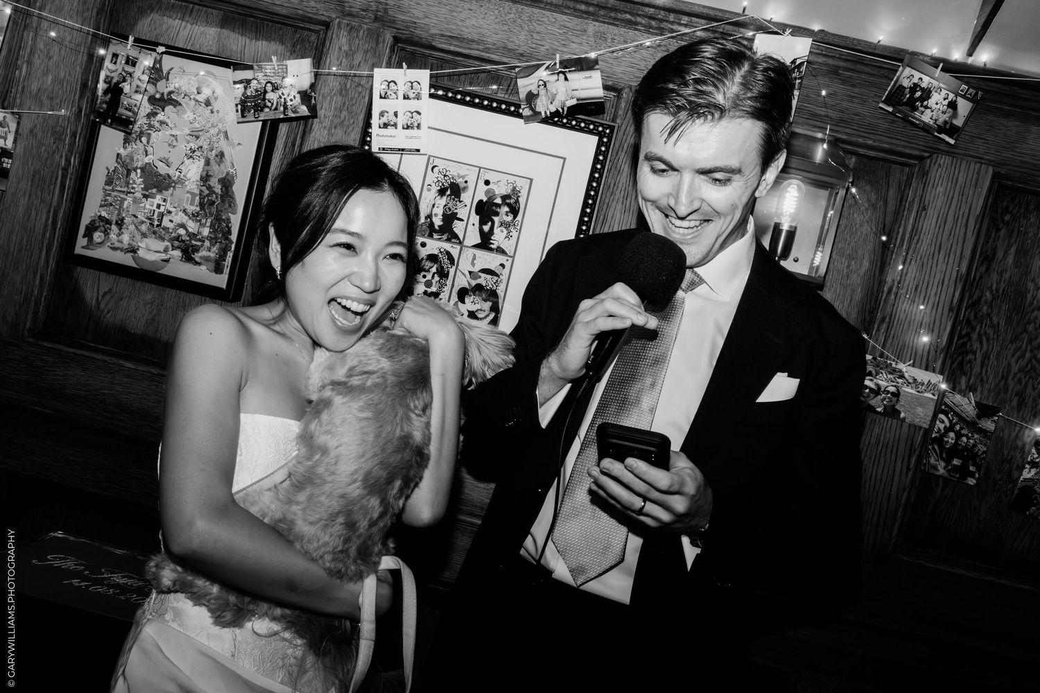 Black and white photo of a laughing bride and groom looking at a phone during their wedding reception.
