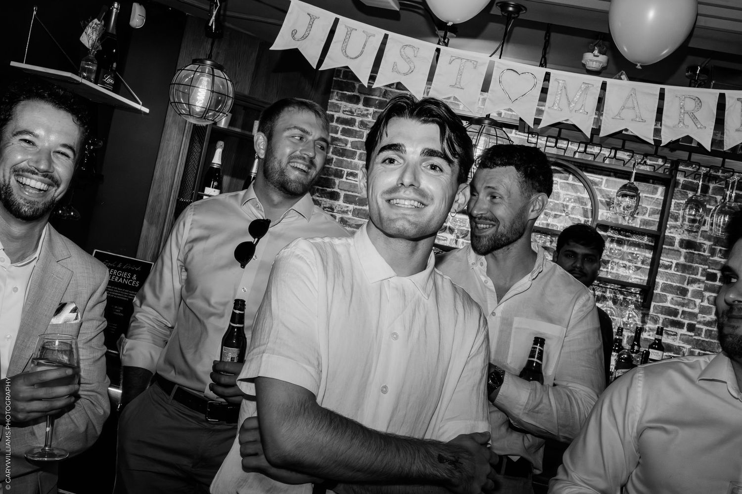 Black and white photo of men laughing and holding drinks at a lively indoor party celebration.
