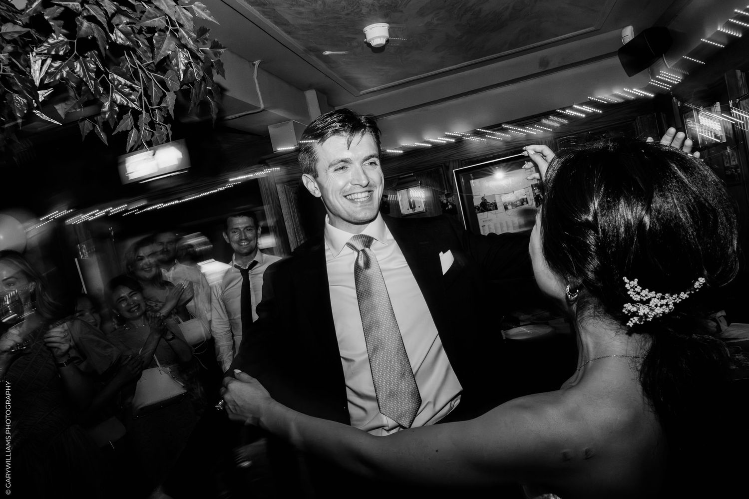 Black and white photo of a groom smiling while dancing with bride at wedding reception.