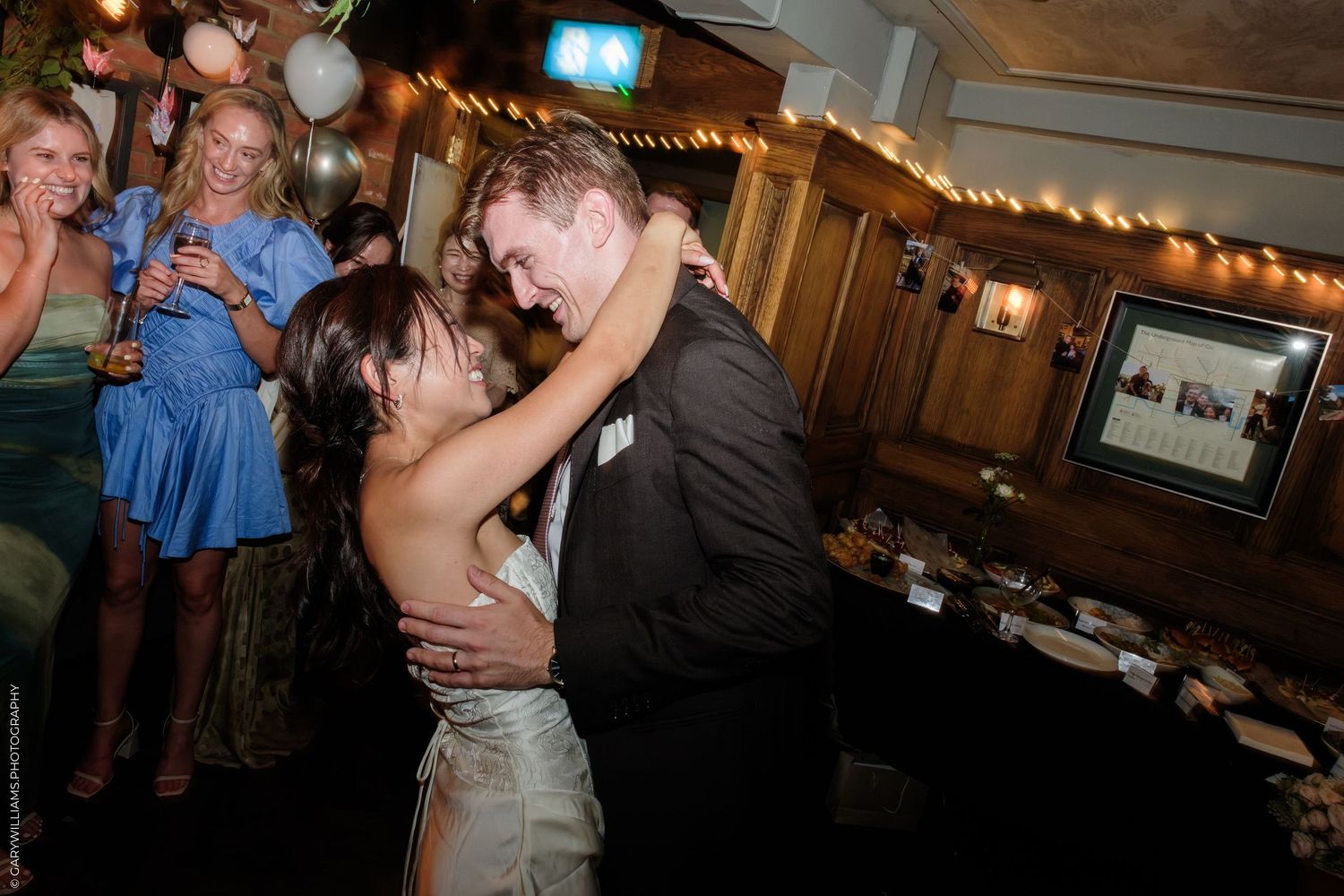 Couple sharing a romantic dance at a wedding reception while guests celebrate in the background.