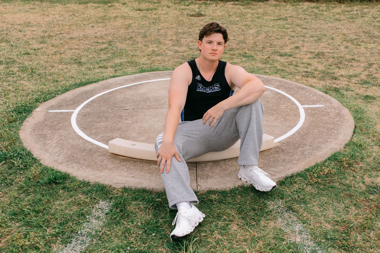 Young athlete stands in discus throwing circle holding a discus, wearing a Knights jersey, black and white photo.