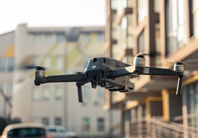 A DJI drone flying in an urban environment with apartment buildings in the background on a sunny day.