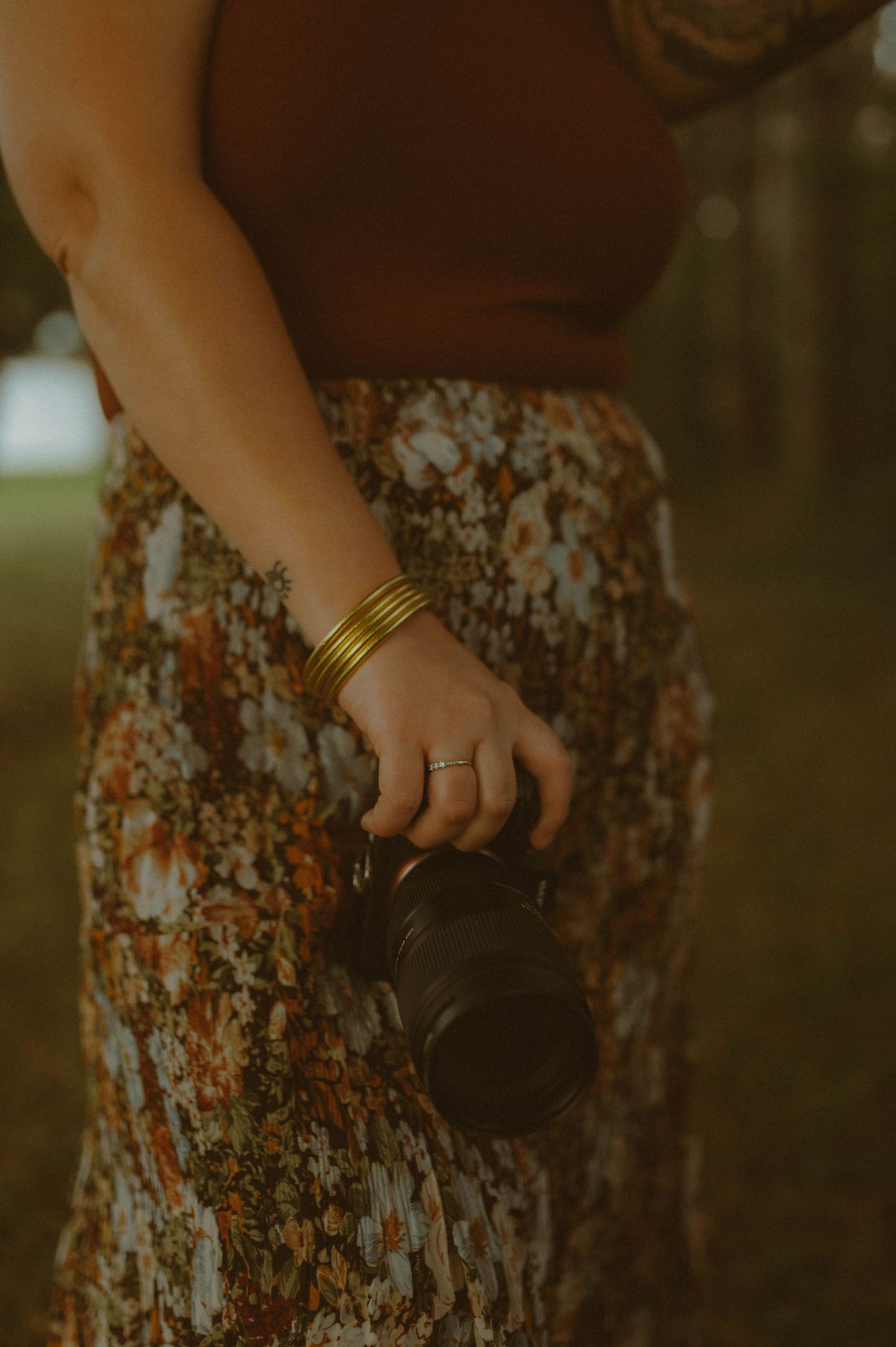 Close-up of a woman holding a camera with gold bangles and a floral skirt.