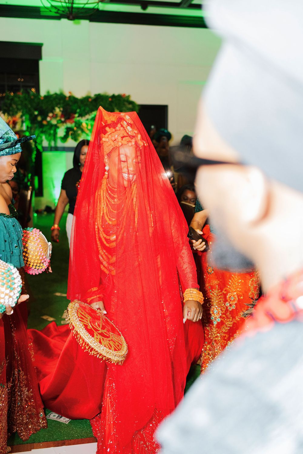 A bride in a stunning red veil and traditional attire walks through a ceremonial procession at a cultural wedding.