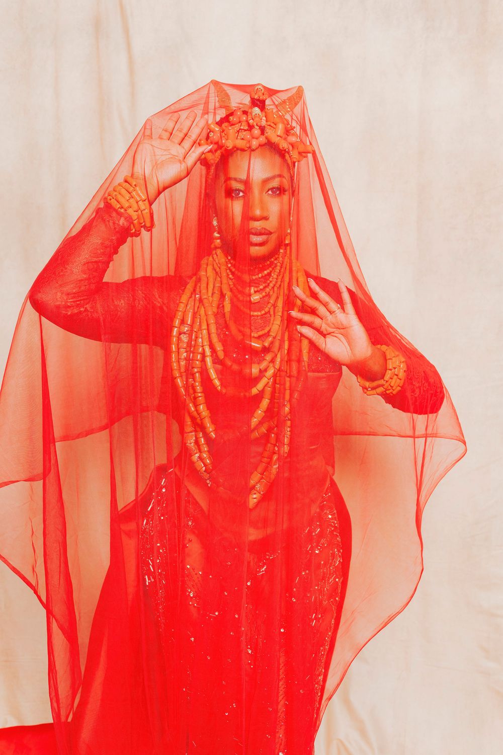 Woman in vibrant red ensemble with sheer veil, floral crown, layered beaded necklaces, and ornate bracelets posing elegantly.