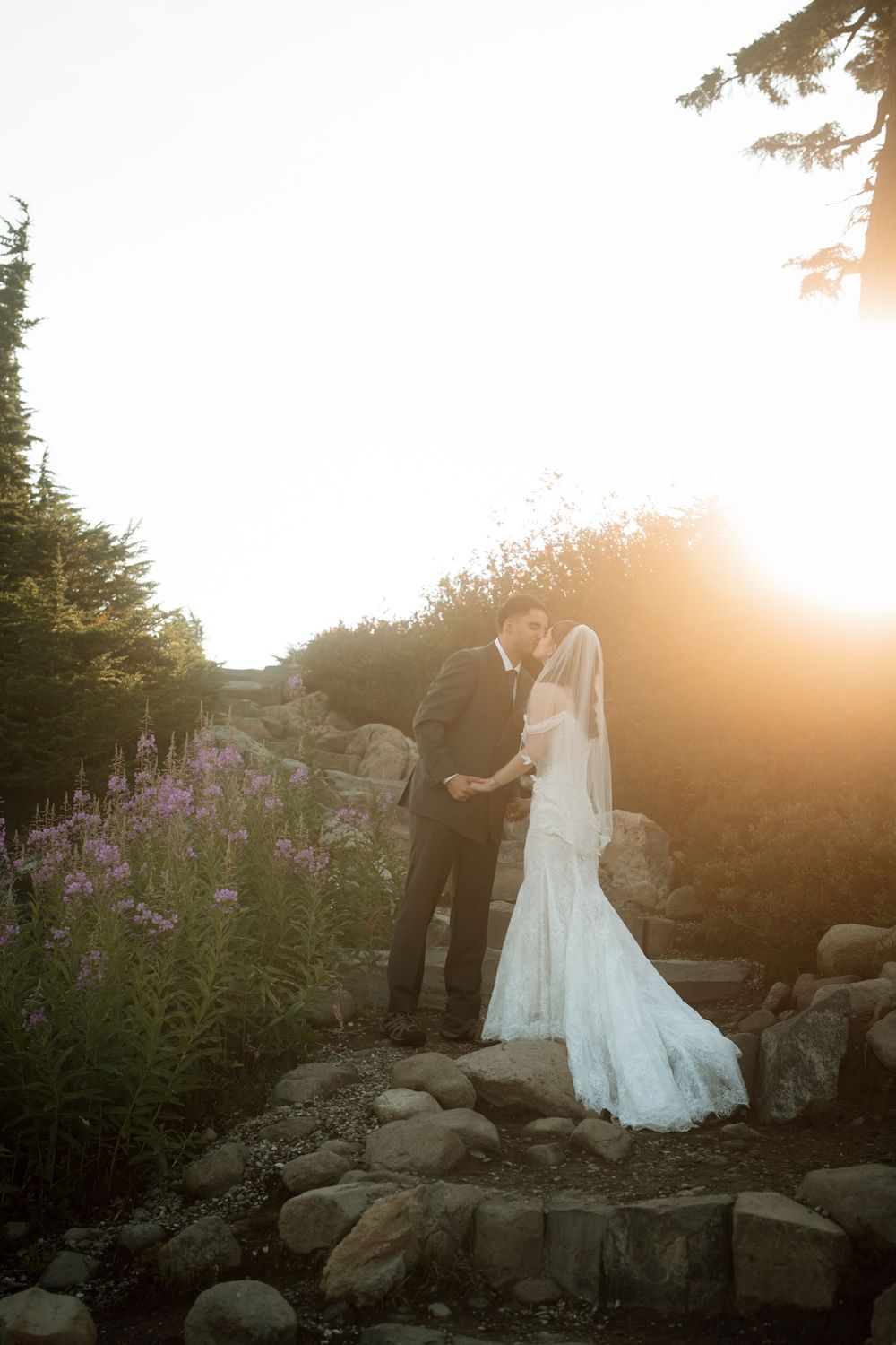 Bride and groom share an intimate moment among wildflowers and rocks during a golden sunset outdoor wedding.