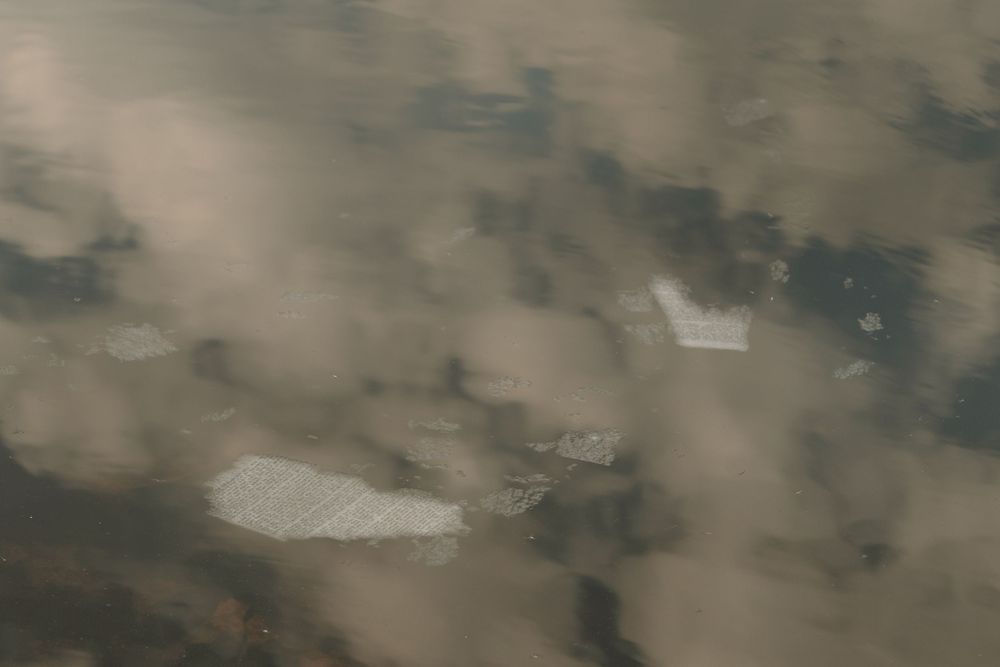 Aerial view of misty landscape with patches of snow and dark terrain visible through clouds.