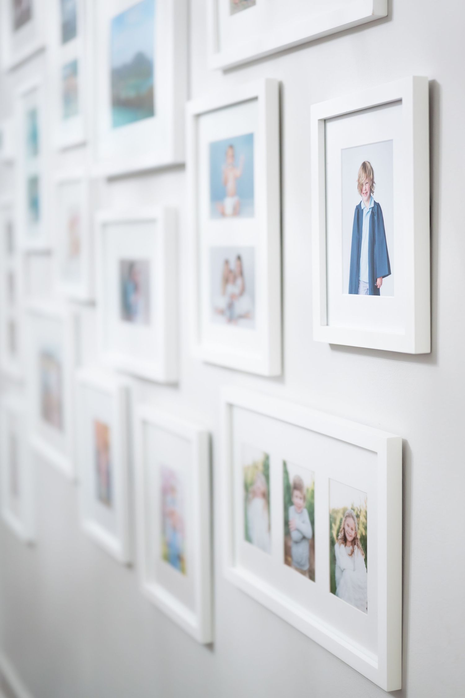 White-framed family photos arranged in a gallery wall display on a bright white wall.