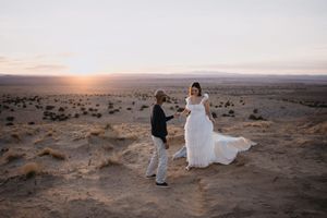 Couple in wedding attire sharing a romantic moment at sunset in a vast desert landscape.