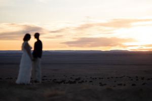 Silhouetted couple holding hands at sunset in a vast desert landscape with golden sky.