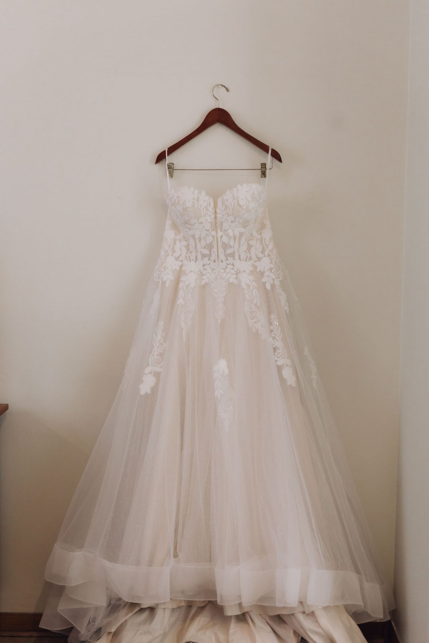 Elegant strapless A-line wedding dress with lace bodice and tulle skirt hanging on wooden hanger.
