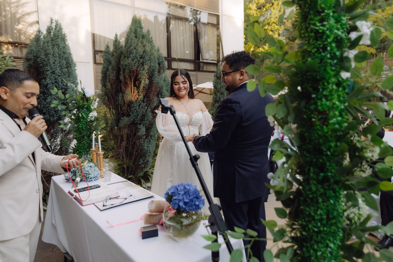 Couple exchanging vows at outdoor wedding ceremony with officiant and floral decorations.