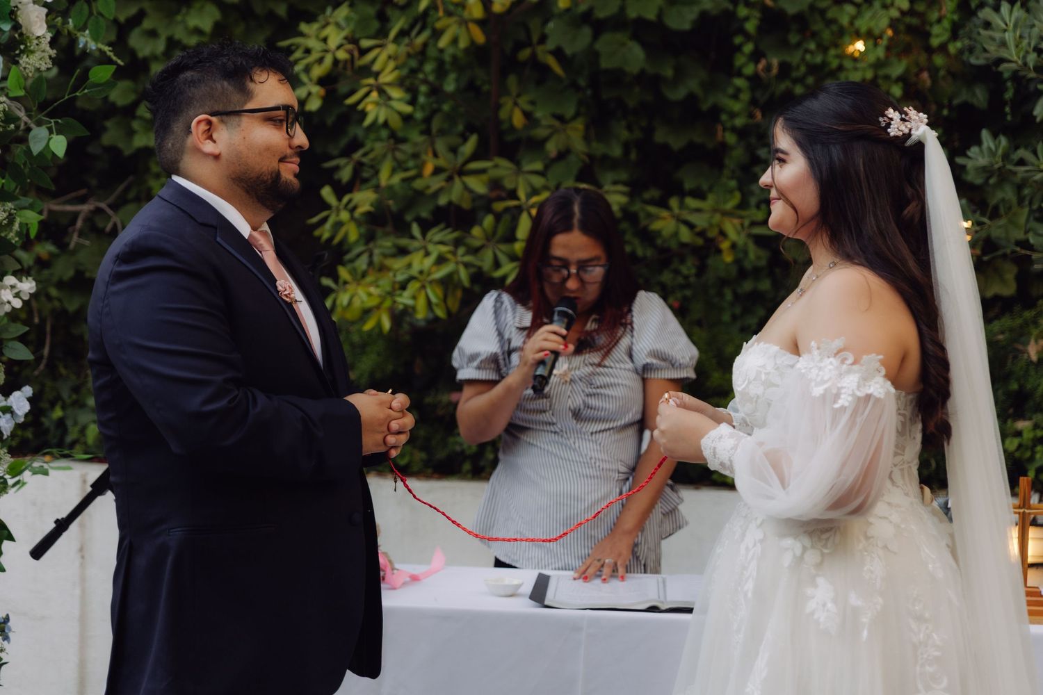 Bride and groom exchanging vows with red cord binding ritual at outdoor wedding.