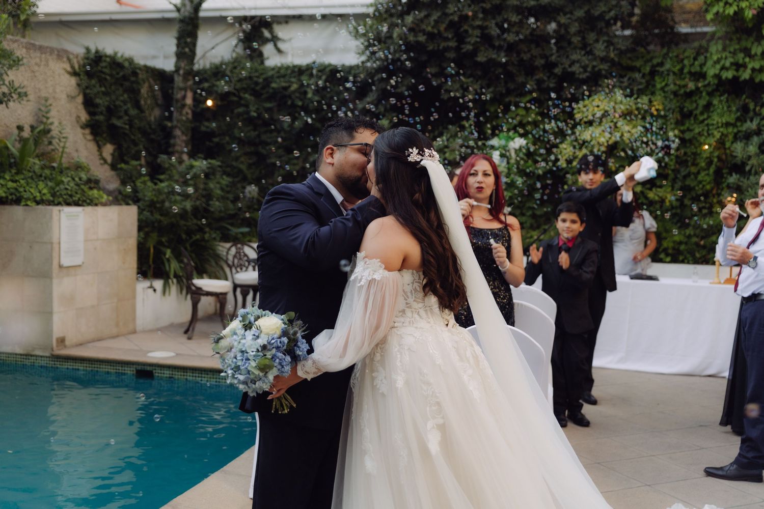 Bride and groom share a joyful moment during outdoor wedding ceremony by pool with confetti.
