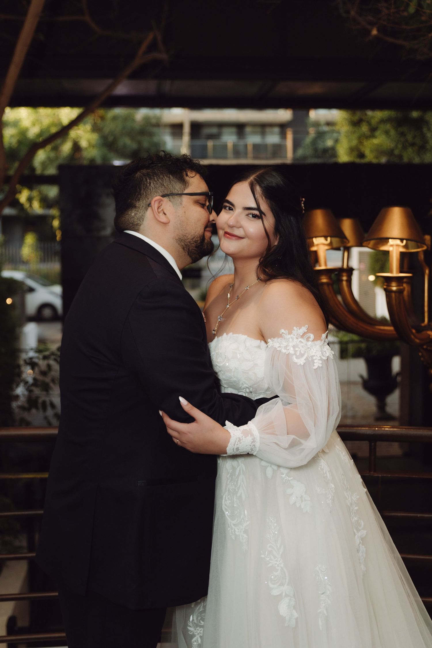 Bride and groom embrace tenderly near elegant candlelit chandelier at wedding venue.