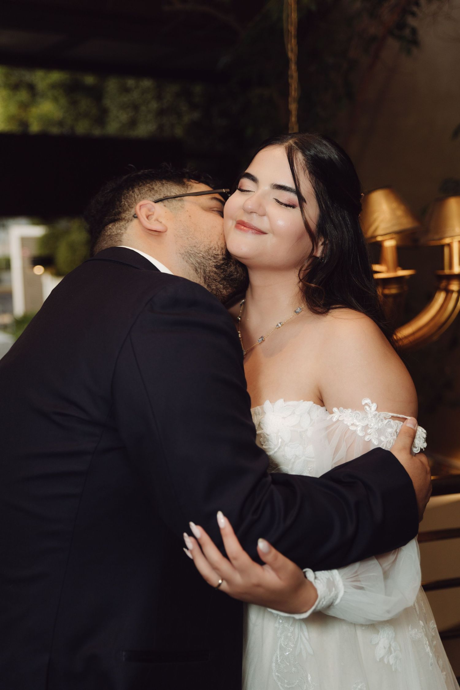 Groom kisses bride on cheek as she smiles blissfully during wedding celebration.