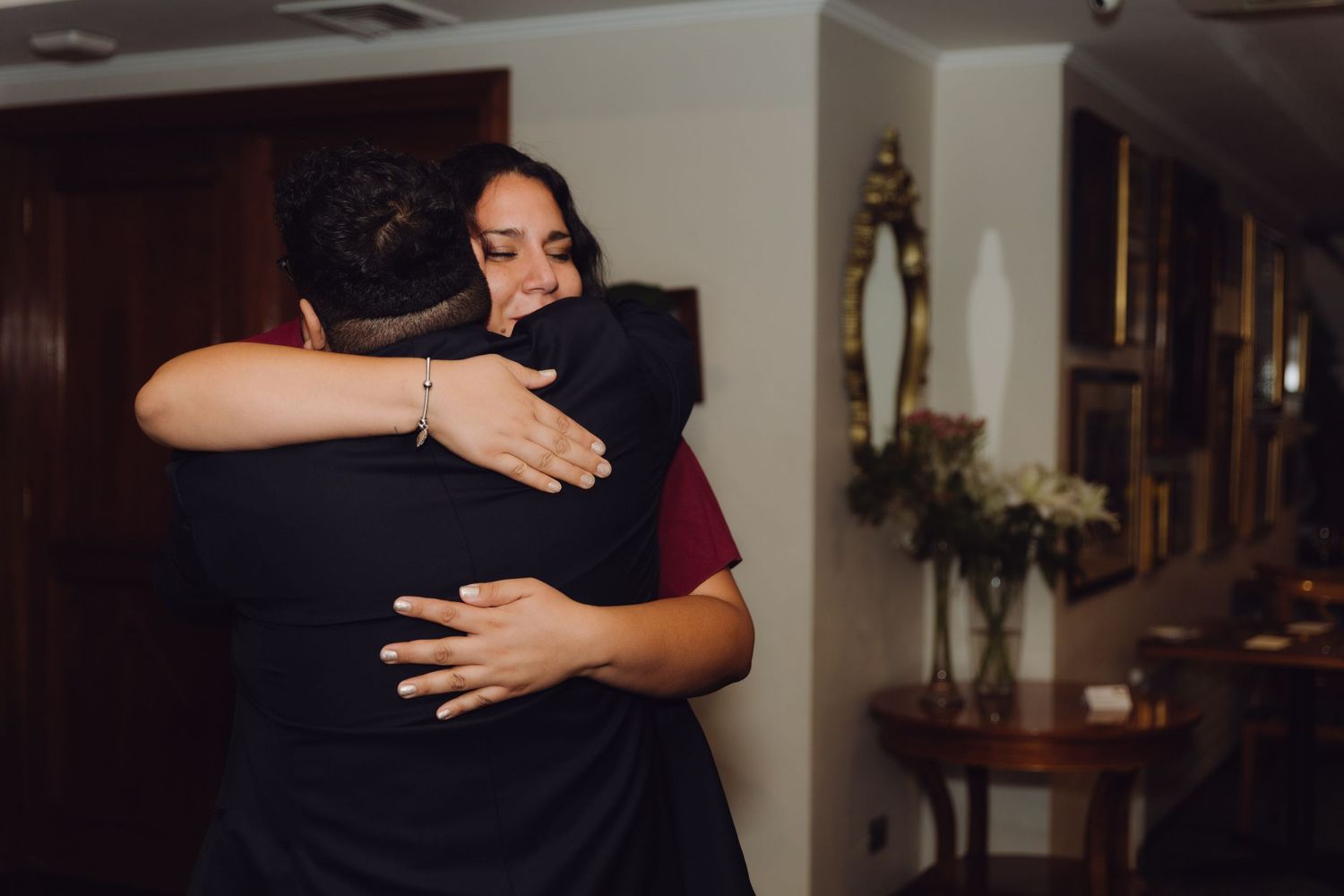 Woman in burgundy dress sharing heartfelt hug with guest at wedding celebration.