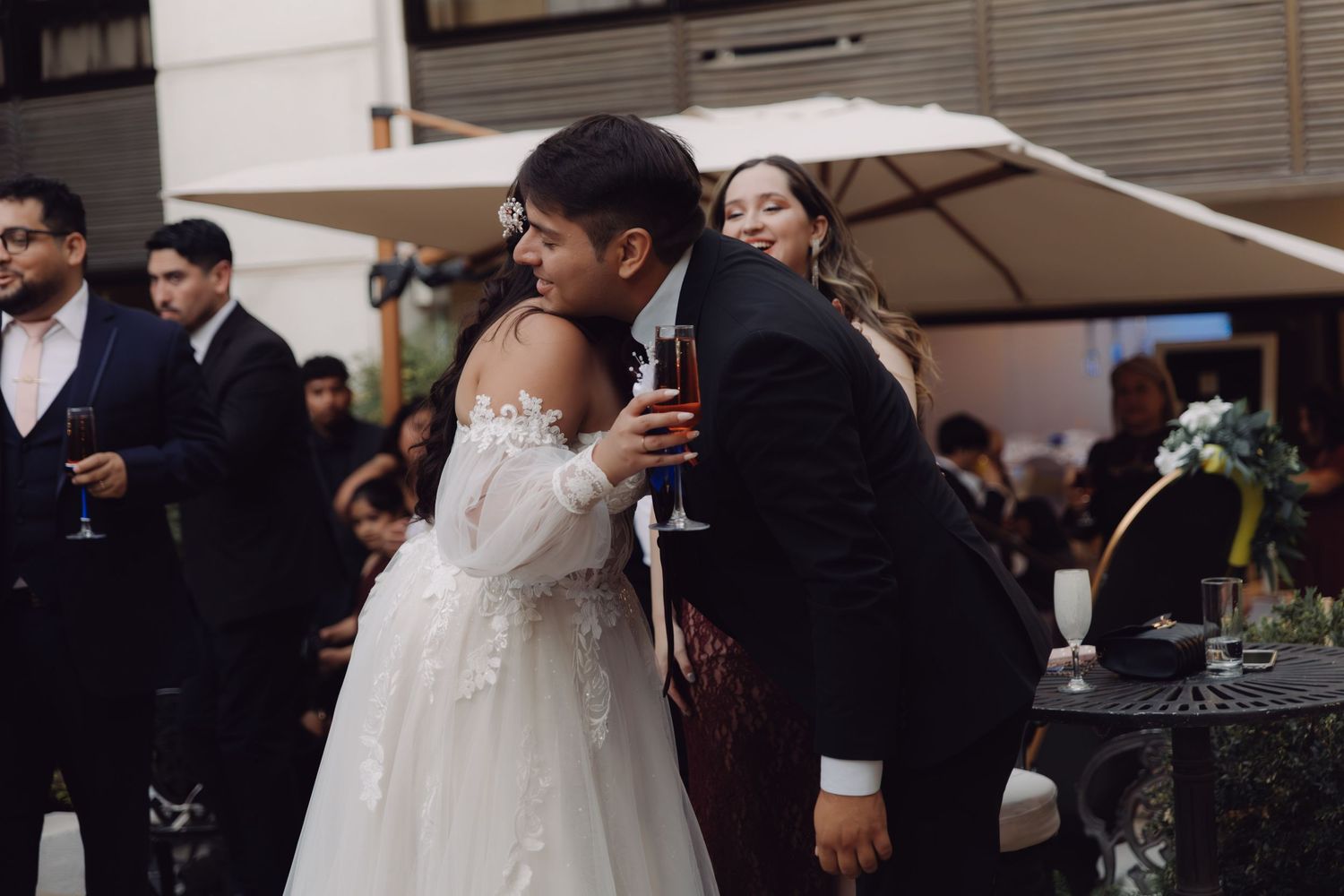 Bride in white gown and groom in suit sharing tender moment at outdoor reception.