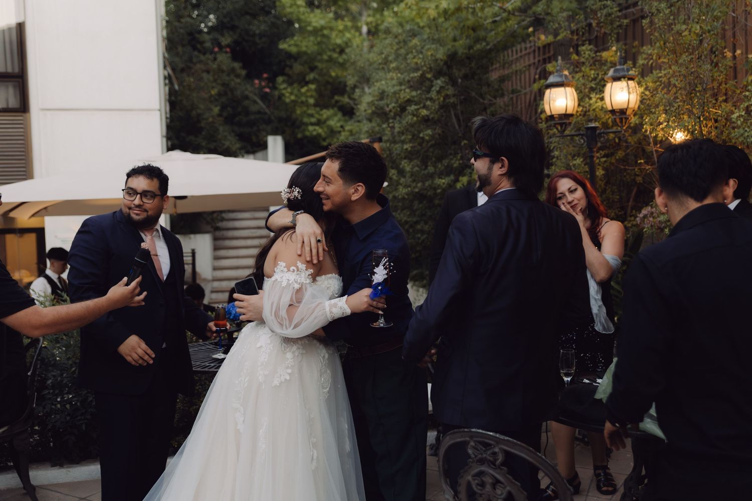 Bride in white dress receiving congratulatory hug from guest at outdoor wedding.