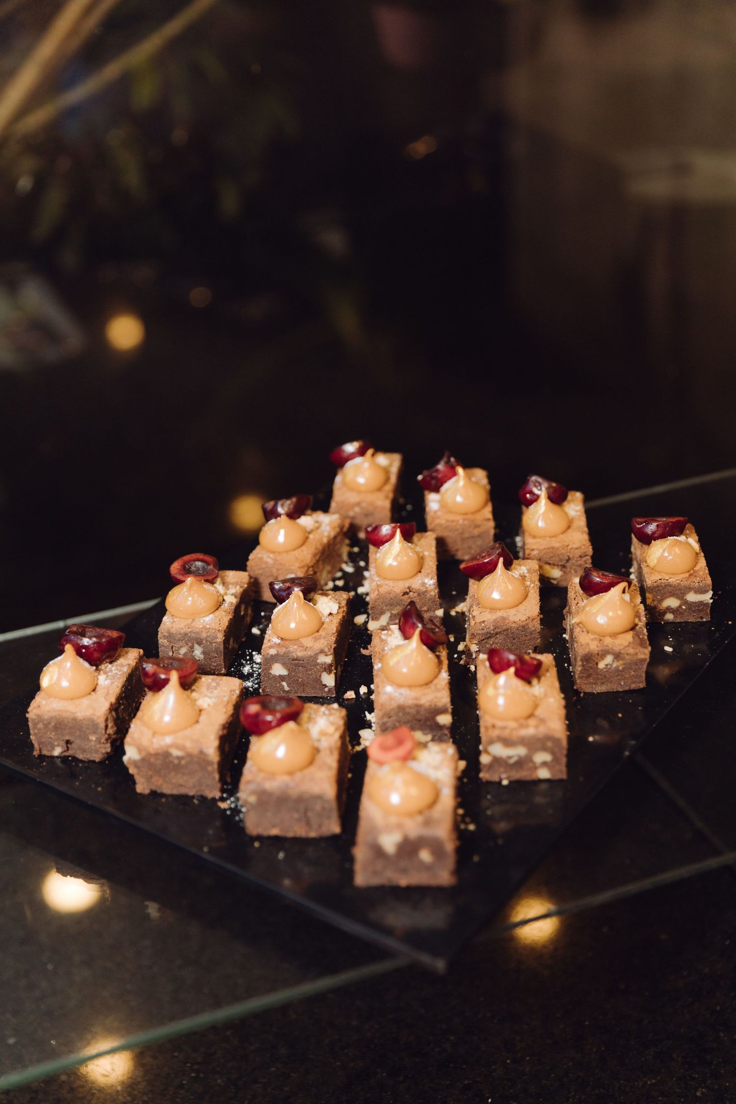 Elegant bite-sized dessert squares topped with cream rosettes and pomegranate seeds arranged on a dark serving tray.